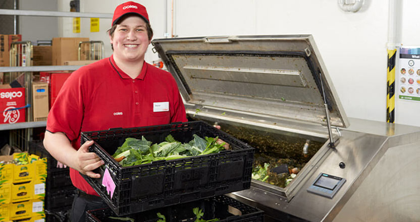 Coles employee holding food waste next to a food processor 