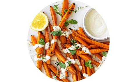 A plate of roasted carrots with tahini dressing and lemon wedges