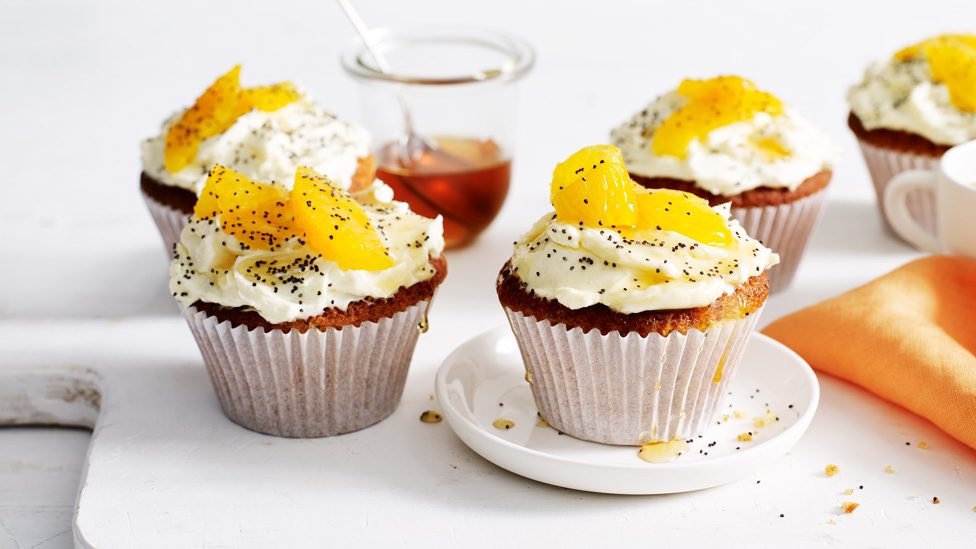 Four orange and poppy seed muffins with cream cheese icing