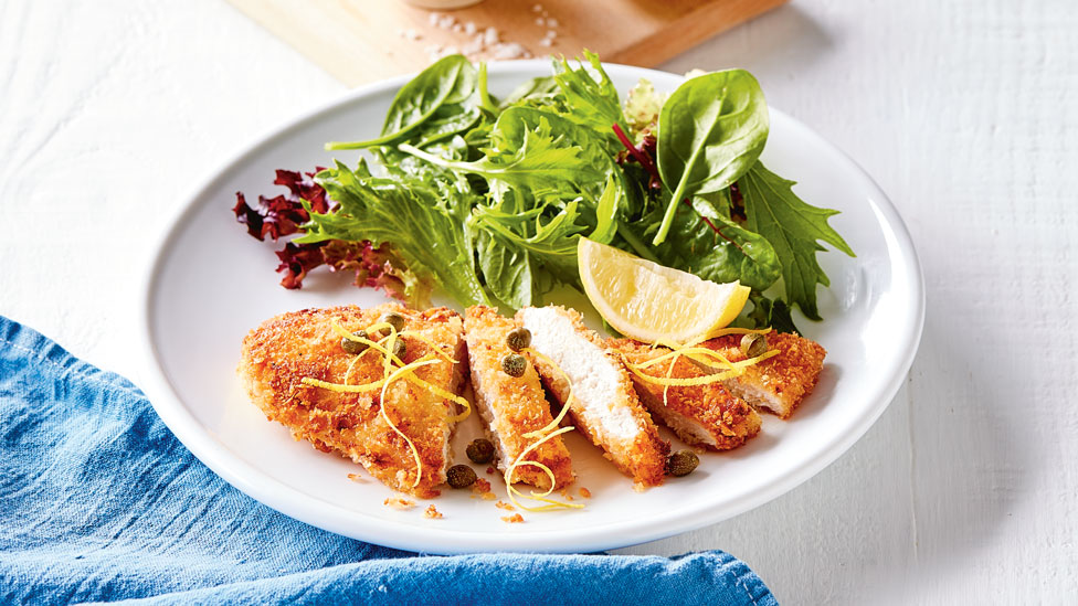 Zesty chicken schnitzel with salad leaves and lemon wedges