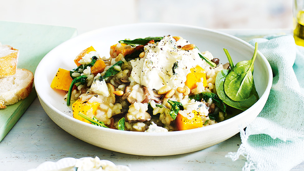 Risotto with pumpkin, mushroom and spincah served in a bowl with basil on top