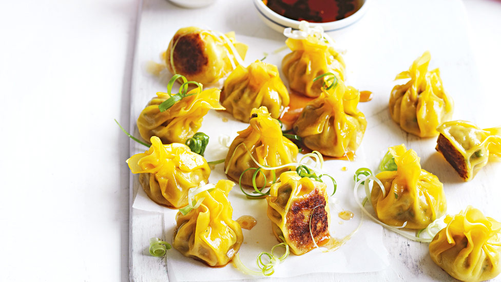 13 pork dumplings with spring onion on top and dipping sauce on the side