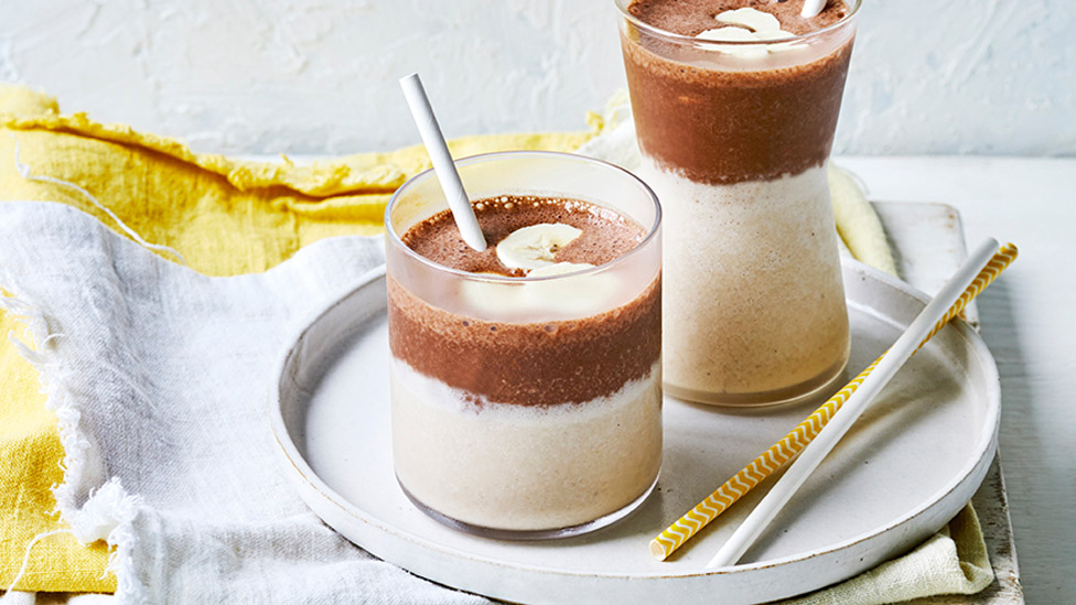 Two cups of chocolate and banana smoothies with sliced banana on top