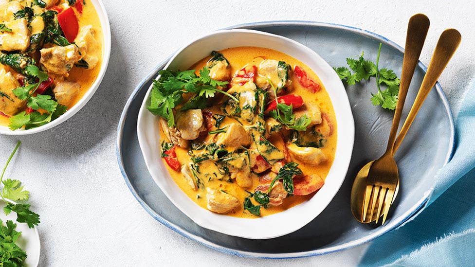 Two bowls of red chicken curry with coriander