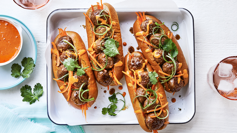 Four meatball banh mi topped with corriander and dipping sauce on the side