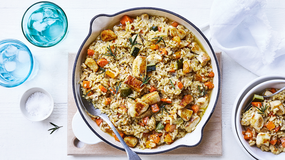 Chicken and vegetable risotto served in a baking dish and a bowl with two glasses of water on the side