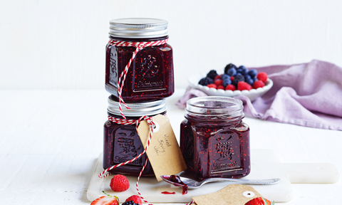 3 jars of mixed berry jam with raspberries and blueberries scattered around the jars