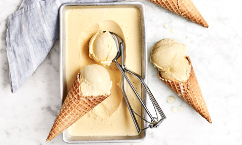 Tub of vanilla ice cream with two cones beside