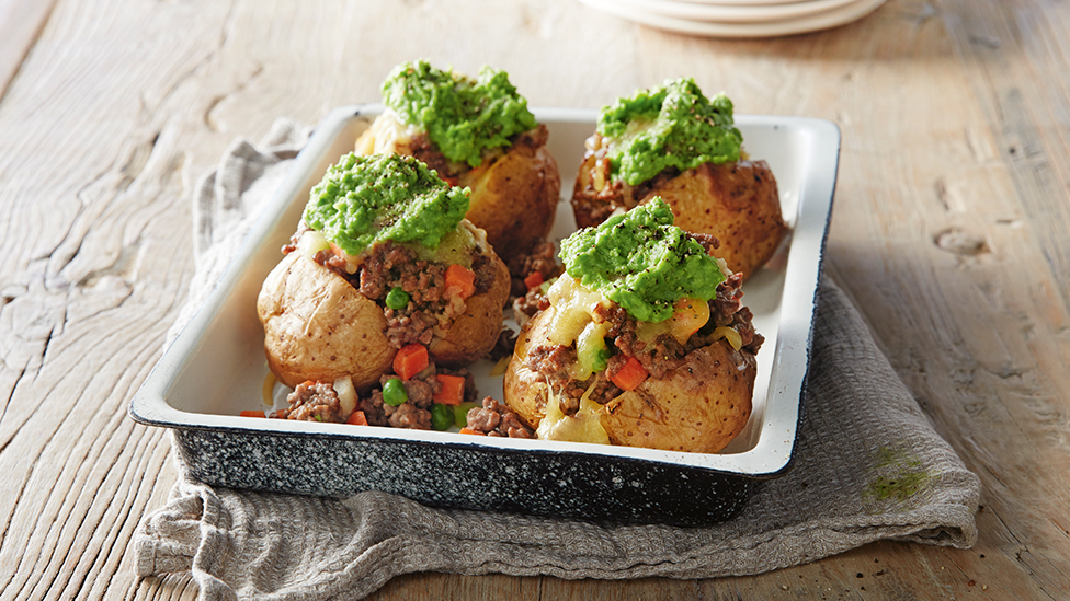 Baked potatoes in a tray, topped with mince and mashed peas