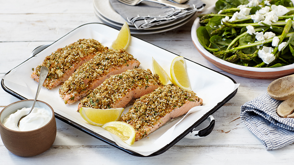 Four salmon fillets topped with dukkah, plus lemon wedges, on a serving plate