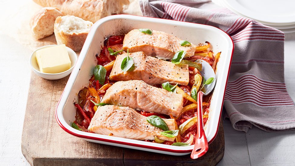 salmon fillets atop pepperonata in a baking dish, sprinkled with basil leaves