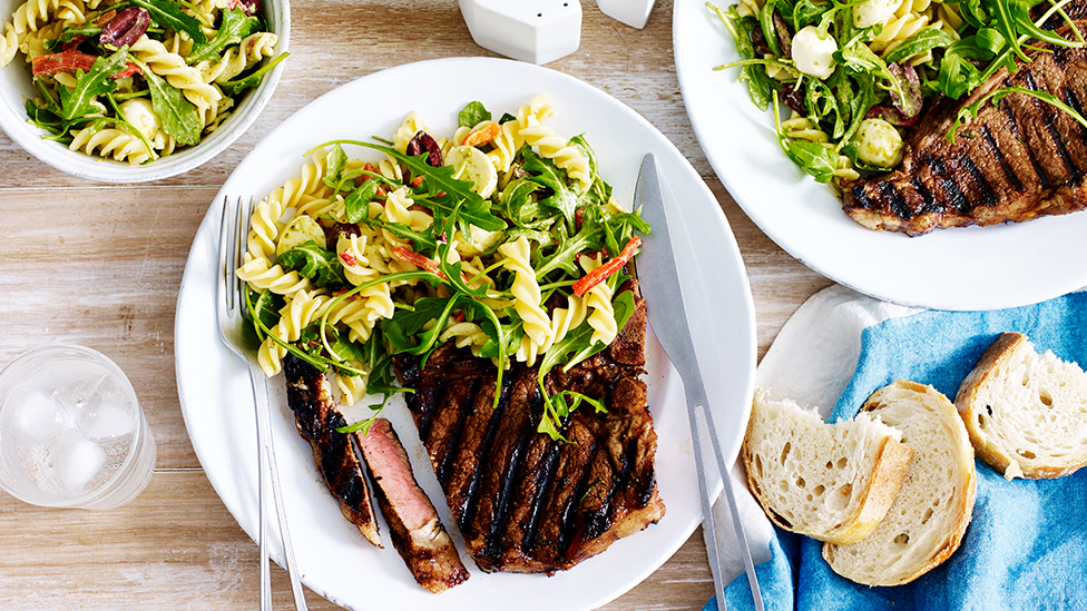 Steak served with a spiral pasta salad on a plate.