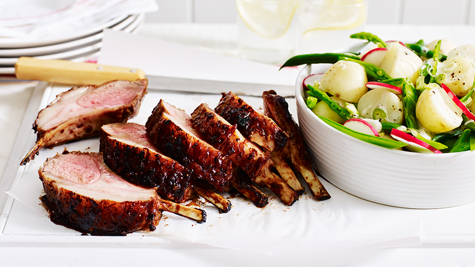 Sliced rack of lamb, on a serving plate with a potato, bean and snowpea salad in a bowl