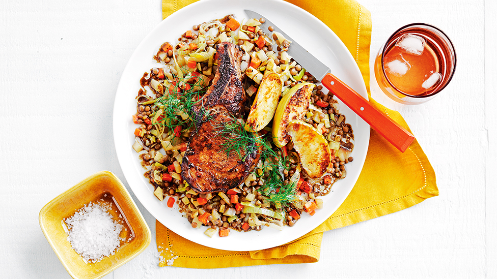 Pork cutlets and cooked apple slices atop a bed of lentils on a serving plate