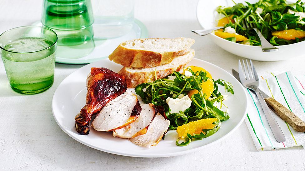 Roasted chicken pieces on plate served with a rocket and orange salad, and crusty bread.