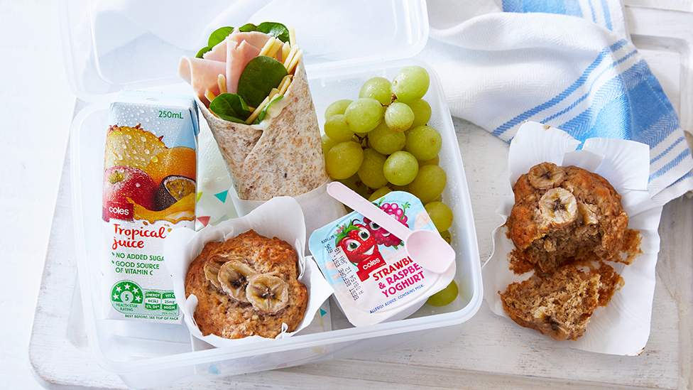Lunchbox filled with a yoghurt tub, juice box, banana muffin, grapes and a wrap