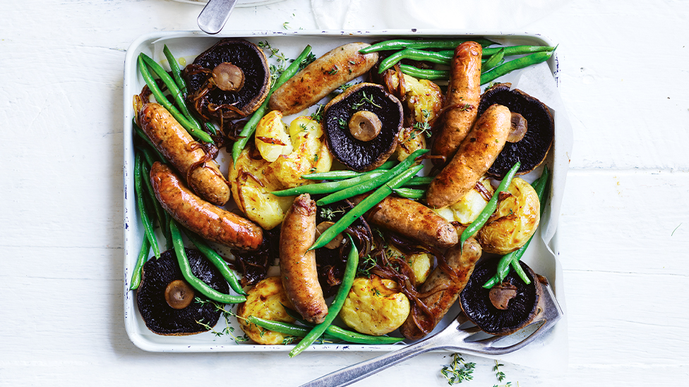 Sausages, potatoes, whole mushrooms and green beans in a baking tray