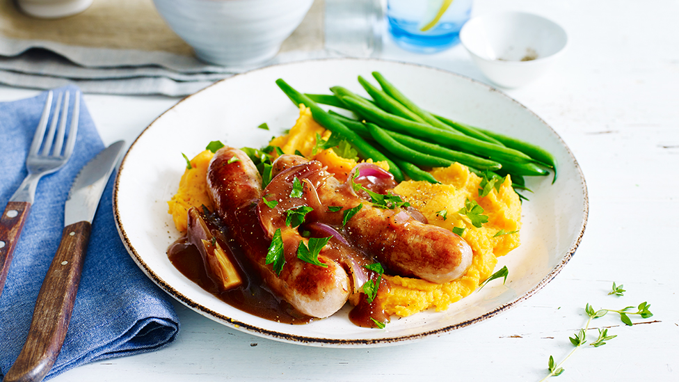 Sausages with onion gravy served with sweet potato mash and green beans on a plate