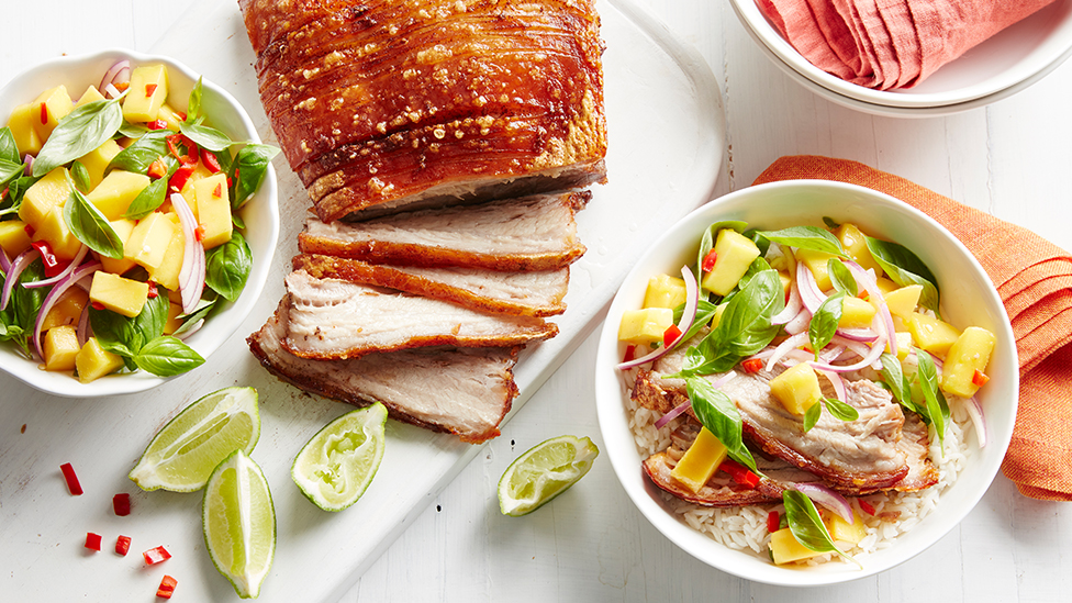 sliced pork on a board, with bowls of mango salsa and rice.