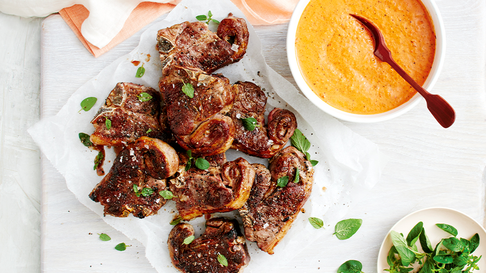 barbecued lamb chops on a plate with a bowl of romesco sauce on the side
