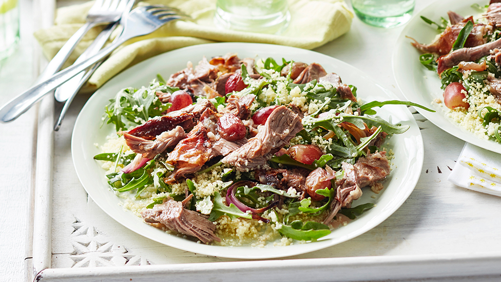 A salad of cous cous, shredded barbecued lamb, rocket, onion and grapes on a plate