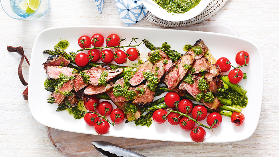 Sliced barbecue steak on a bed of asparagus, topped with cherry tomatoes and salsa verde