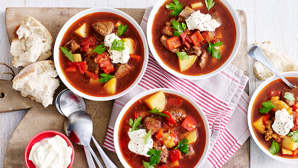Bowls of beef goulash served alongside bread and a bowl of sour cream