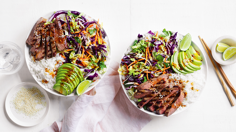 Two bowls of barbecued beef, rice, avocado and salad 