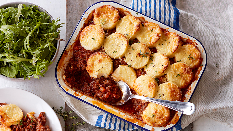beef ragu topped with semolina gnocchi in a baking dish