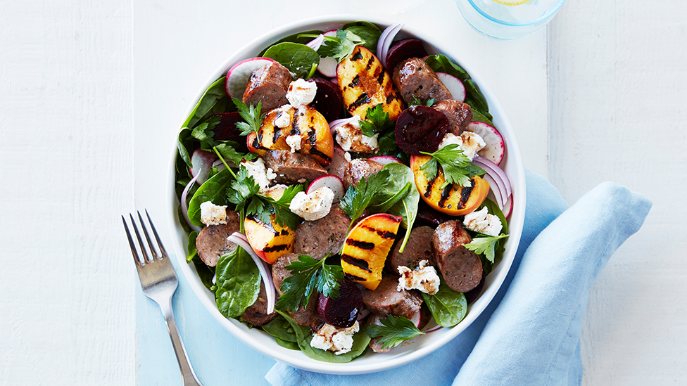 salad of baby spinach, goat's cheese, grilled peach, beetroot and sliced sausage in a bowl