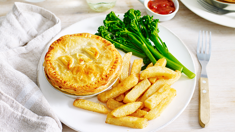 A meat pie decorated with the word DAD on a plate with oven fries and broccolini