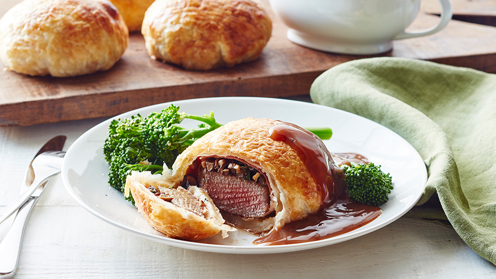 Beef wellington on a plate, served with broccolini and beef gravy