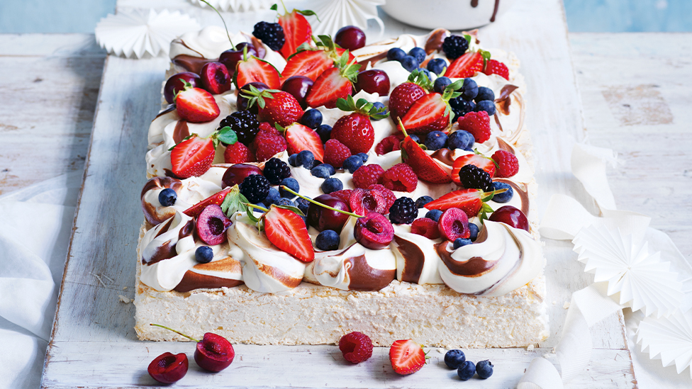 Pavlova topped with chocolate swirled cream, mixed berries and cherries, on a board