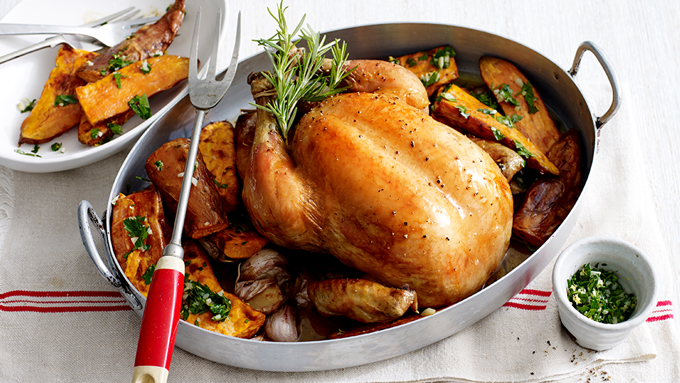 Whole roast chicken a baking dish, surrounded by sweet potato tossed with gremolata