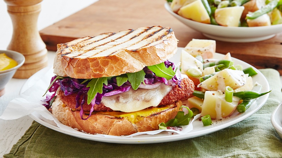 Chicken schnitzel sandwich on toasted bread served with potato salad