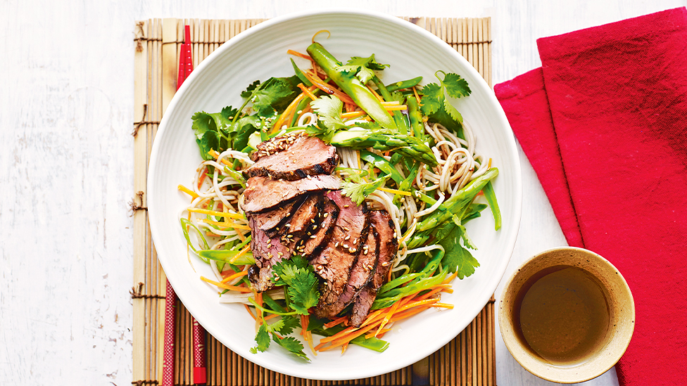 Soba noodle and vegetable salad in a bowl topped with beef slices 