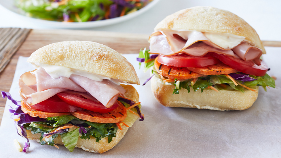 Two bread rolls filled with ham, tomato, grilled sweet potato and salad