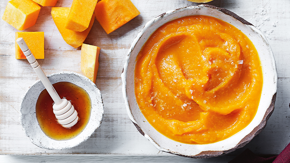 Bowl of mashed pumpkin on a board with a bowl of honey and raw pumpkin pieces