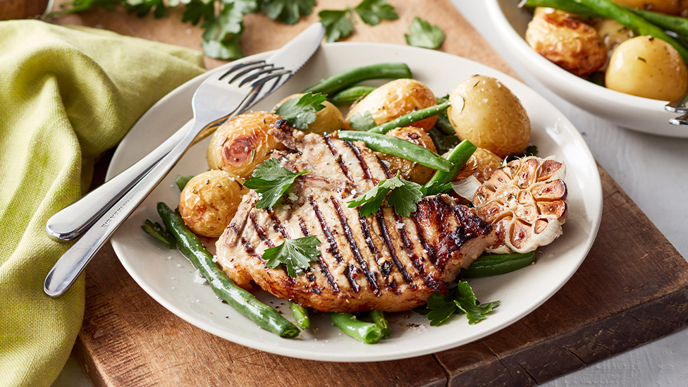 pork cutlet on a plate with roast potatoes, green beans and garlic