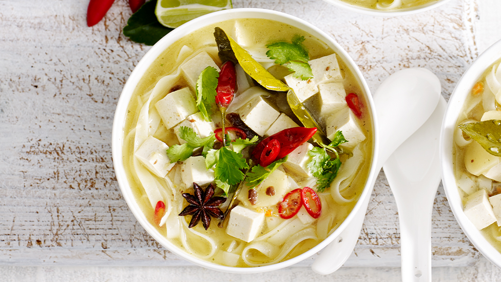 Bowl of hot and sour tofu and noodle soup sprinkled with sliced red chilli and fresh coriander