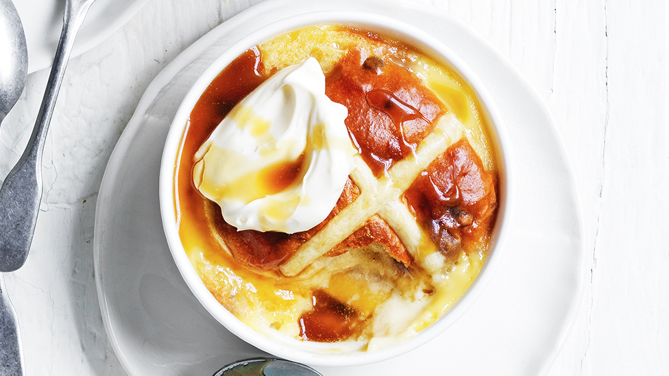 A hot cross bun and apple pudding in a ramekin, topped with a dollop of cream