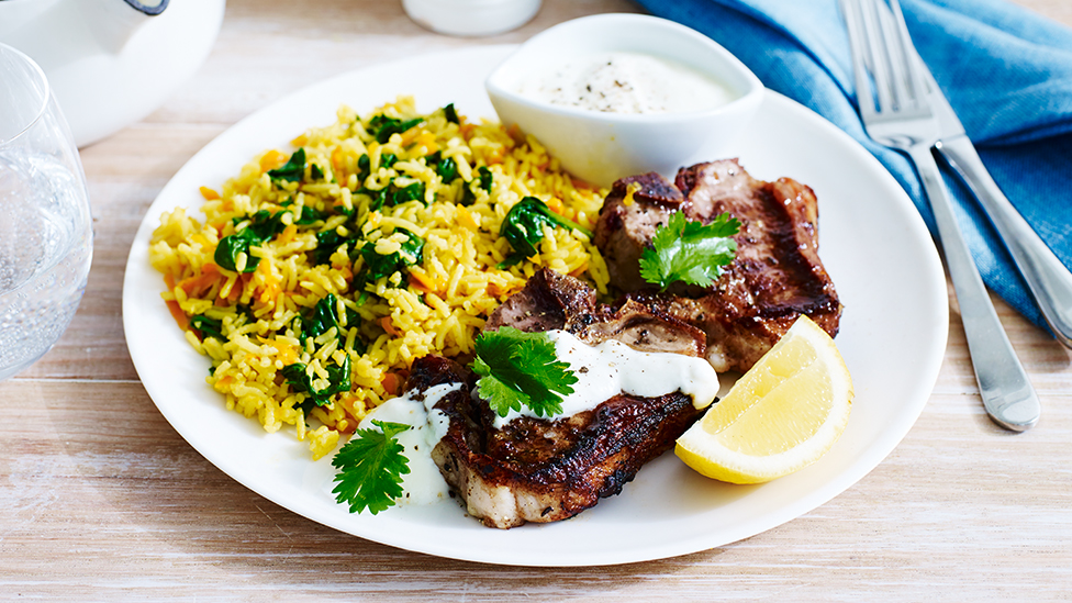 Two barbecued lamb chops on a plate with carrot, almond and baby spinach pilaf