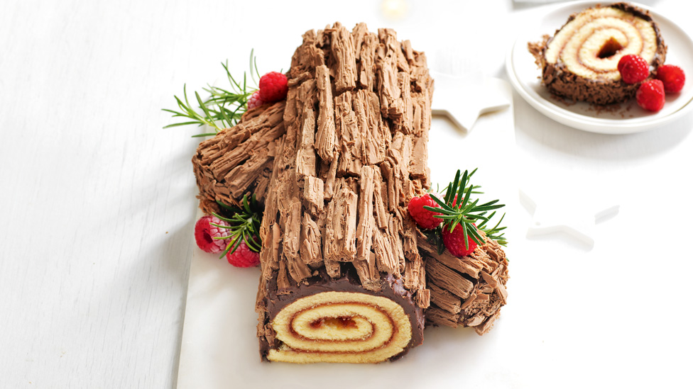 Cheat’s yule log decorated with rosemary sprigs and raspberries
