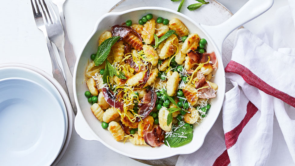 Pan-fried gnocchi with peas and crispy pancetta, garnished with mint leaves and lemon zest.