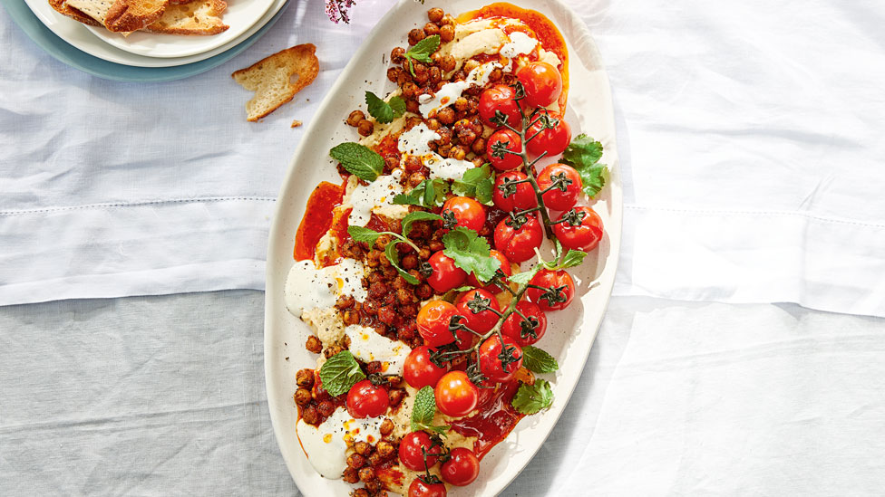 A tray of loaded hommus topped with chickpeas and roast tomatoes