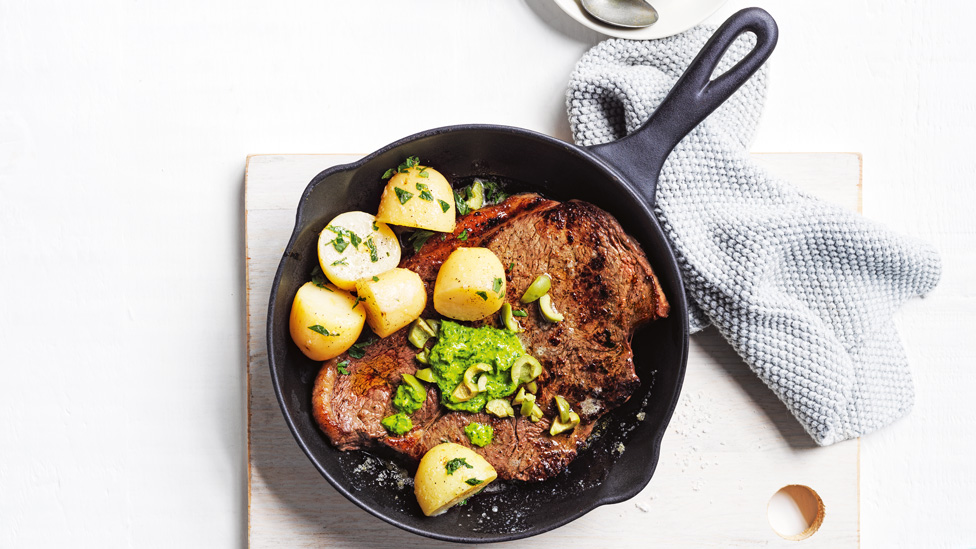 Pesto and olive steak served with potatoes in an iron skillet 
