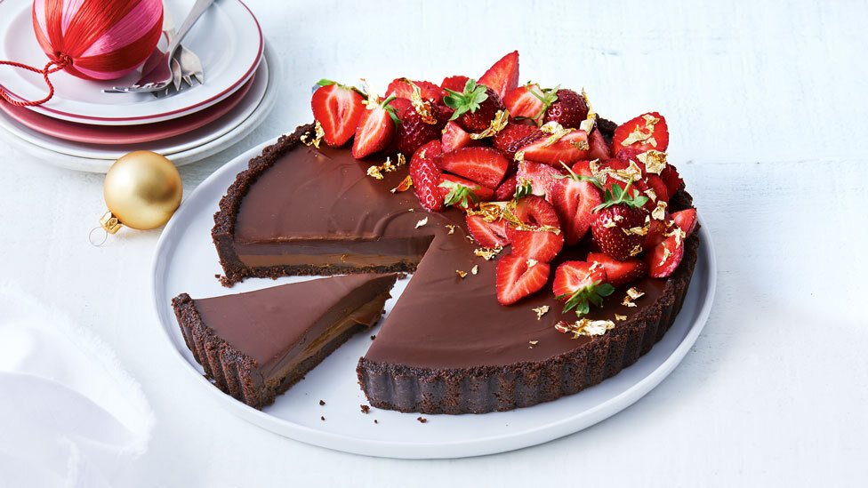 Salted caramel and Choc Ripple tart with a slice cut out, garnished with fresh strawberries.