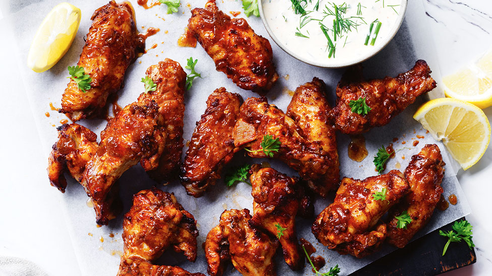 A tray of spiced chicken wings with ranch dressing, lemon and some parsley