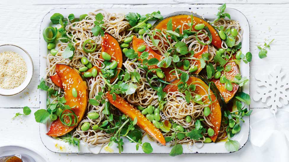 Teriyaki roasted pumpkin and noodle salad on a serving dish, garnished with spring onion curls and toasted sesame seeds.