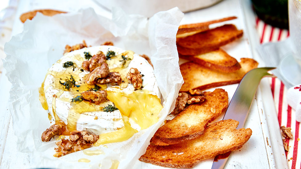 A baked brie cheese with thyme and walnuts on top, served with crispy bread